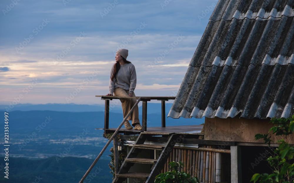 Fototapeta premium A woman sitting on wooden balcony and looking at mountain views on cloudy morning