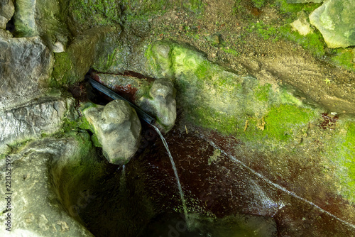 Natural spring water flowing steadily from a simple pipe among moss covered rocks in a quiet forested canyon near the ancient troglodyte village, Khndzoresk, Armenia