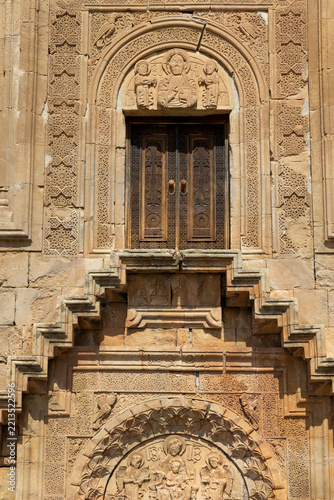 Ornately carved stone entrance with sculpted saintly figures and tympanum relief above the wooden door of Surb Astvatsatsin church and monastery, Noravank, Armenia