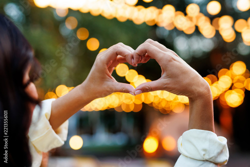 Woman making heart hand gesture in front of warm bokeh lights