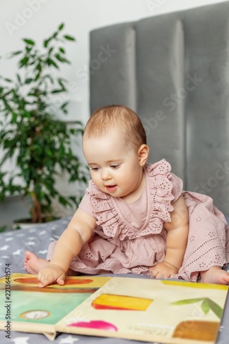 Baby girl pointing at colorful picture book on bed