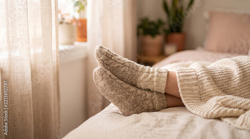 Cozy feet in thick knitted socks resting on a bed with soft blankets  