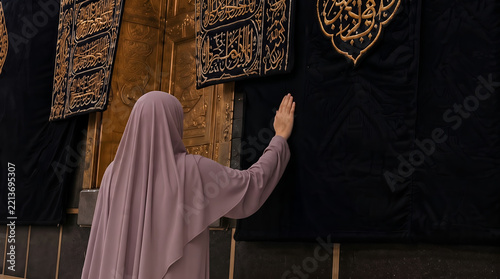 Muslim woman in hijab touching the black cloth of the Kaaba during