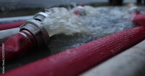 Water coming out of high-pressure red and white fire hoses along a city street during emergency flooding operations