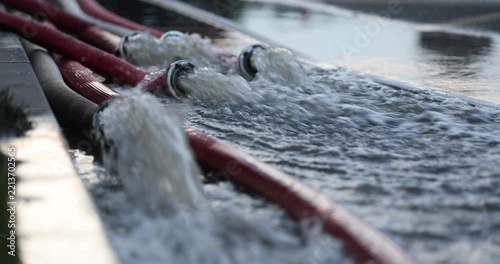 Water coming out of high-pressure red and white fire hoses along a city street during emergency flooding operations