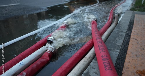 Water coming out of high-pressure red and white fire hoses along a city street during emergency flooding operations