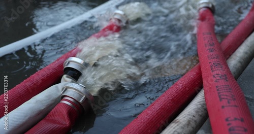 Water coming out of high-pressure red and white fire hoses along a city street during emergency flooding operations