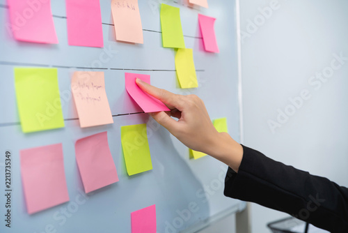 Person organizing colorful sticky note on whiteboard during brainstorming or planning session at modern office workspace