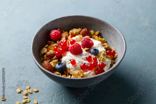 Healthy granola bowl with yogurt and fresh berries on dark teal background. Close up.