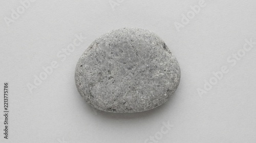 Single smooth gray pebble viewed from above on minimal light grey background