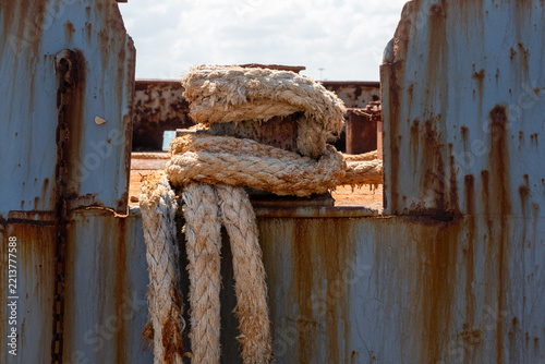 Rusted Mooring Rope Wrapped Around Single Bollard on Grey Ship Hull in Crete
