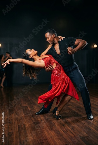 Professional couple dancing salsa in a dark studio with wooden floor