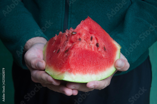 Delicious slice of watermelon in hand with a blurred background.