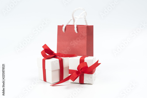 Small white wrapped gift boxes decorated with red ribbons alongside a red paper shopping bag. Perfect for Christmas sales, Valentine's Day, holidays, and promotional retail shopping concepts.