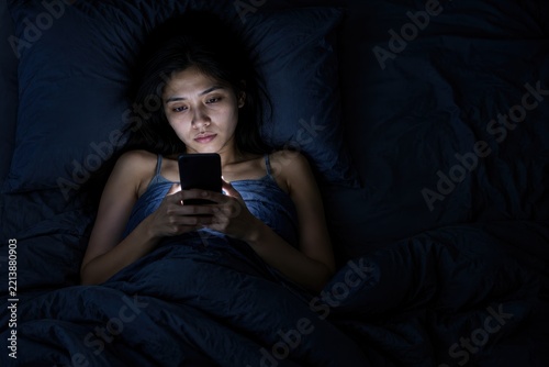 Woman lying awake in bed at night scrolling on glowing smartphone