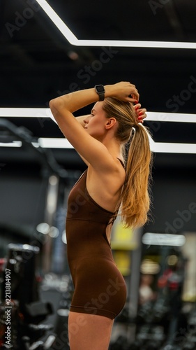 Athletic woman adjusting her ponytail while standing in a modern gym with bright lighting