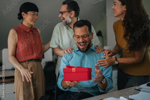 Coworkers celebrating office birthday giving surprised colleague a gift