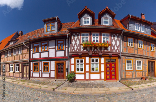 Colorful traditional half-timbered houses with decorative facades, red tiled roofs and flowers along a cobblestone street in Wernigerode, Germany.
