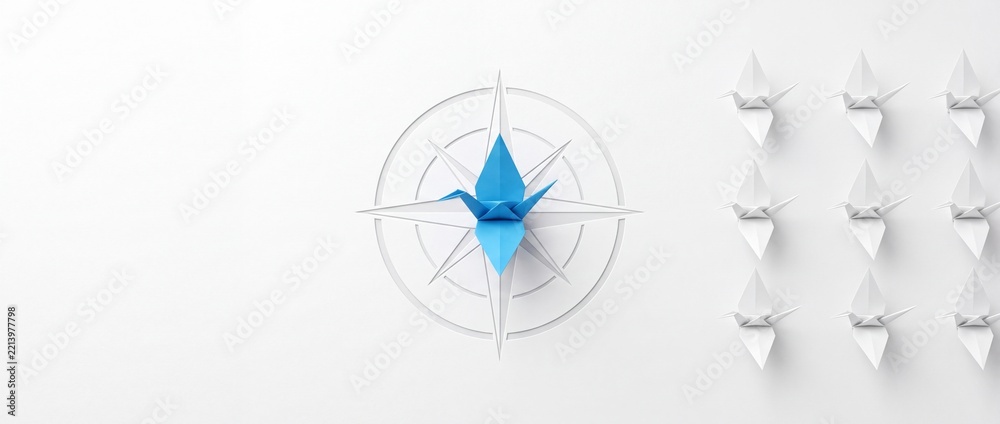 Fototapeta premium Conceptual leadership and direction metaphor featuring a blue origami crane at the center of a compass rose surrounded by a row of white paper birds on a clean white background.