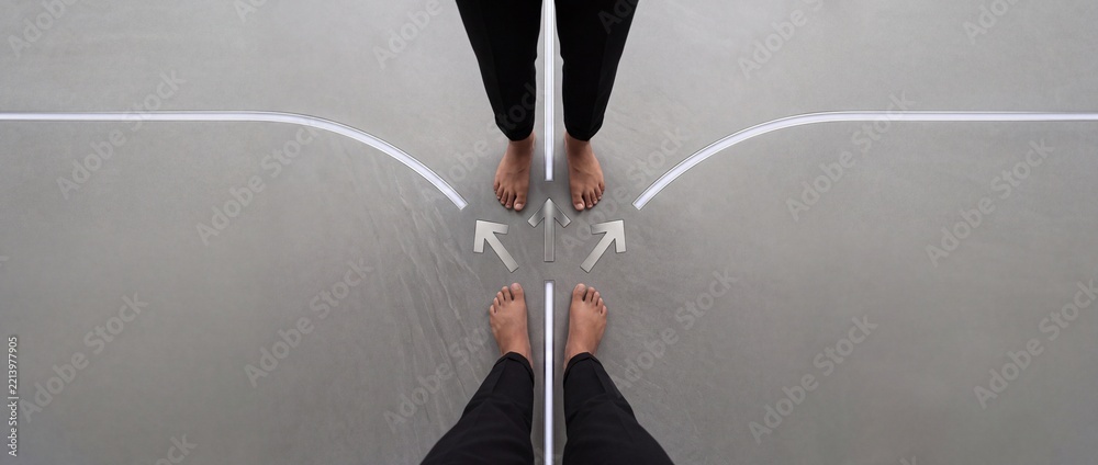 Naklejka premium Minimalist overhead view of two people standing at a symbolic crossroads with glowing arrows and paths, representing business decision making, life choices, and strategic career directions.