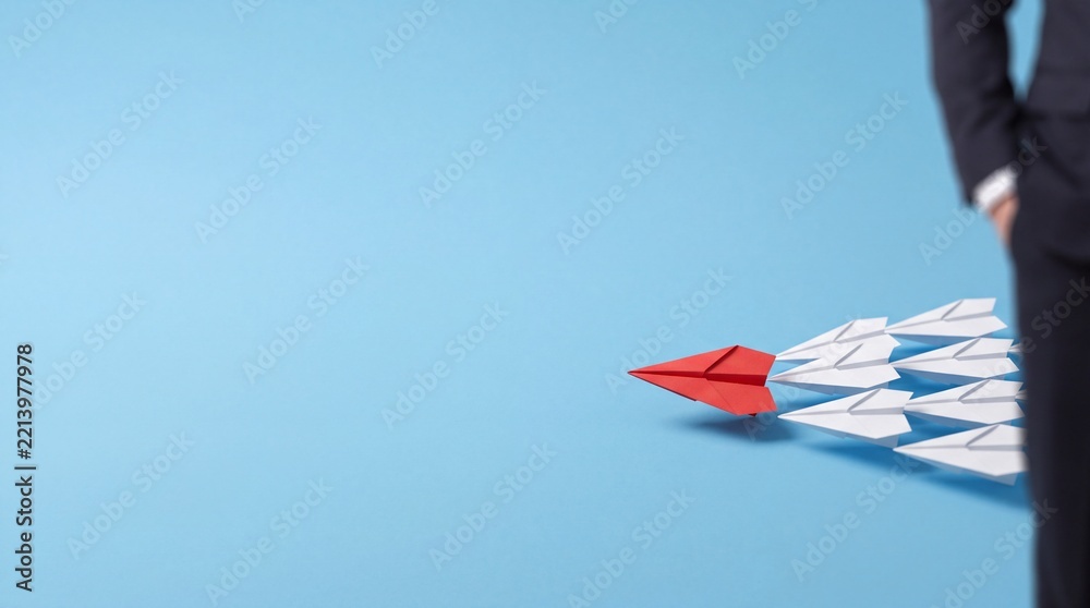Fototapeta premium Red Paper Plane Leading a Group of White Ones Representing Business Leadership and Vision with Large Negative Space for Text on a Blue Background beside a Professional Businessman