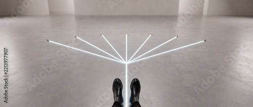 Conceptual first person view of a person in black boots standing at a junction of branching glowing white lines on a concrete floor, symbolizing choice, strategic paths, and future possibilities.