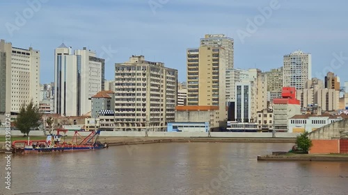 Floating dredge boat anchored in the river near the urban shoreline of Porto Alegre Brazil with tall mid-rise buildings and apartments standing in the background