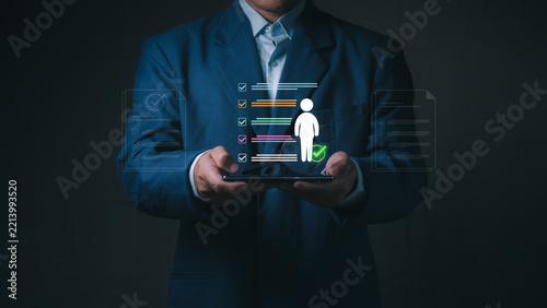 A businessman holds smartphone with approved candidate profile checklist for human resources recruitment, talent acquisition, and employee performance review.