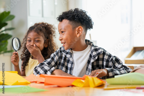 Happy multiethnic school children playing with magnifying glass and paper craft in classroom, cheerful kids having fun in modern classroom with school supplies and magnifying glass
