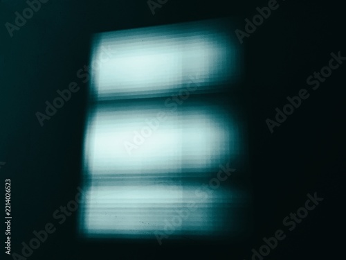 Cyan window light casts a blurry geometric glow onto a dark moody interior wall.
