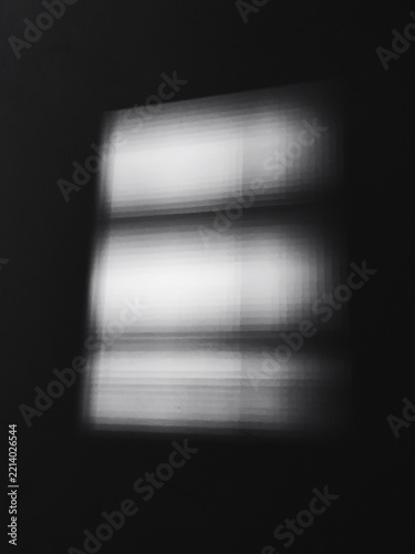 Window light casts a soft blurry rectangular highlight on a pitch black wall.
