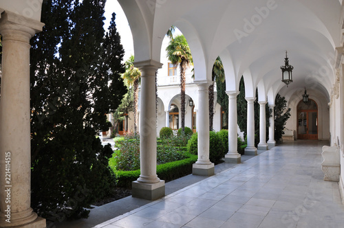 May 26, 2009 - Yalta, Crimea. A beautiful architectural gallery with white arches and a marble floor surrounding a courtyard with manicured plants and palm trees.