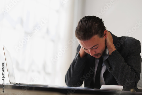 Male professional working on laptop experiencing discomfort and physical pain due to long hours, stress, and fatigue