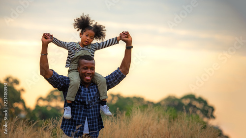 Happy African family child daughter riding the neck father and running on meadow nature on silhouette lights sunset.  Travel and Family Concept, copy space for banner