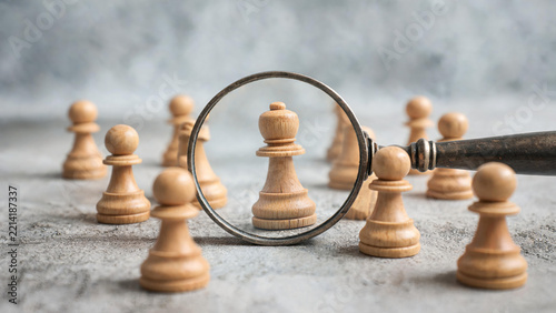 A magnifying glass highlights a unique chess piece among identical pawns, symbolizing selection and focus on outstanding individuals.