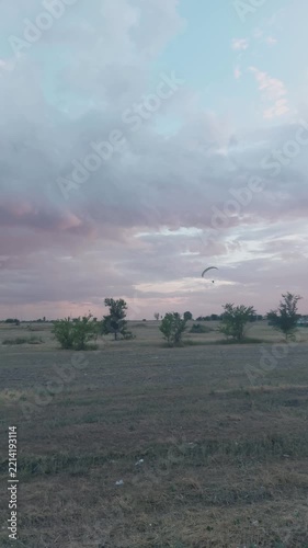 Paraglider soaring over open dry field during colorful sunset with pink and blue cloudy sky