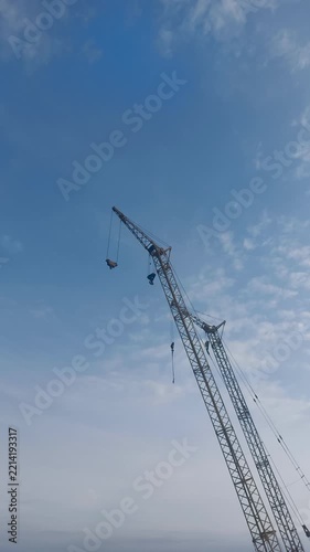 Low-angle shot of a tall lattice boom construction crane against a bright blue sky with scattered white clouds