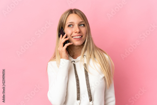 Young blonde woman isolated on pink background keeping a conversation with the mobile phone with someone