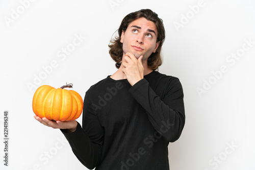 Young handsome man holding a pumpkin isolated on white background having doubts