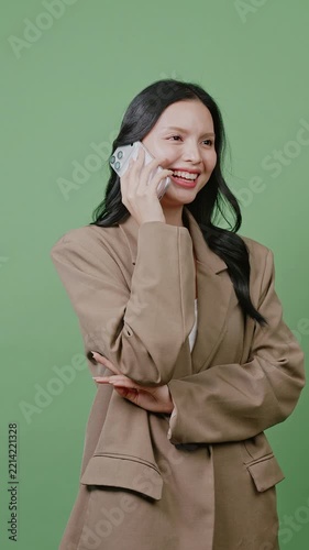 An Asian businesswoman talking happily on her smartphone against a green screen.