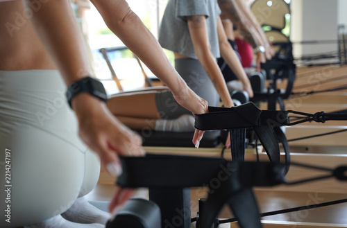 A group of young women perform pilates exercises on reformer machines under the guidance of a coach