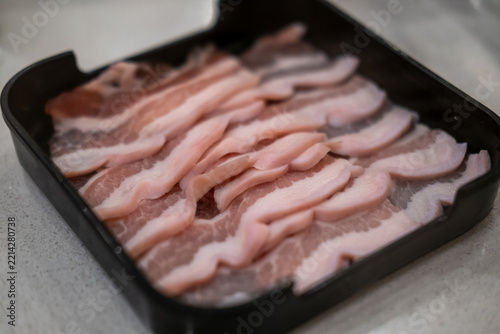 Fresh sliced raw pork belly arranged on a tray, prepared for barbecue cooking.