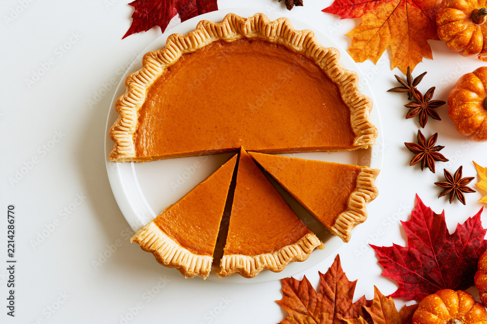 Fototapeta premium Sliced pumpkin pie with autumn leaves, star anise and mini pumpkins, Thanksgiving flat lay