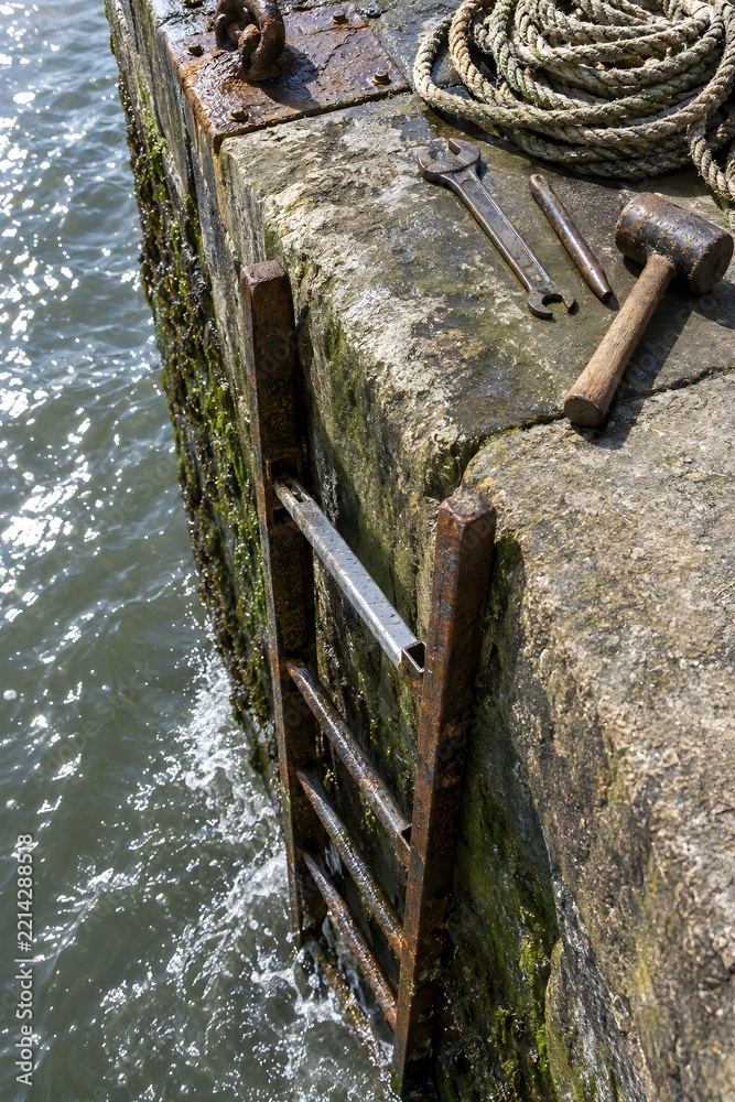 Fototapeta premium A rung removed from an iron ladder set into a river quay wall with the new rung resting in the runner and a spanner