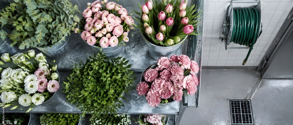 Fototapeta premium Galvanised shelf holding zinc buckets packed with cut blooms in a florist cold room with tiled back wall