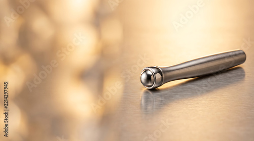 Metal eye roller massager tool on a reflective surface