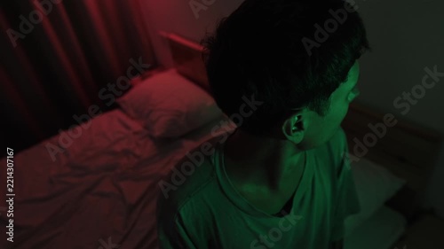 Anxious man nervously looking around his bedroom, scanning the room for danger while expecting a threatening event, expressing hypervigilance, fear and paranoia in red and green low key light