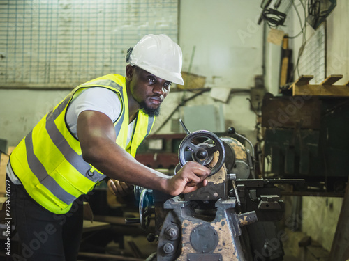 African Machinist Operating Metal Lathe Machine Industrial Workshop : Focus factory technician in white hardhat high-visibility vest operating manual lathe machinery shape metal part
