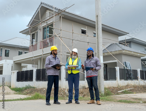 Diverse Engineer Discussing Solar Panel Installation Residential Construction Site: Multiethnic civil contractor hardhat reviewing renewable energy plans blueprint sustainable housing development.
