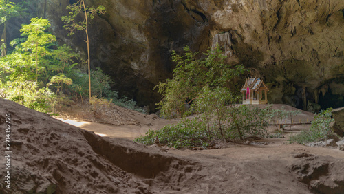 Small ornate pavilion nestled inside a vast limestone cave with lush green trees and sandy floor